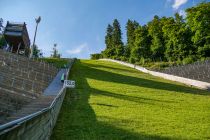 Aufsprunghügel und Mühlenkopf Kraxler - Im Sommer findet jährlich der Mühlenkopf Kraxler statt, während dem sehr sportliche Menschen den sehr steilen Aufsprunghügel hinauf"kraxeln", denn ohne festhalten ist es kaum möglich. Das geht bestenfalls in unter fünf Minuten. Links befindet sich die Treppe. Es sieht einfach aus, aber sie wird von Stufe zu Stufe steiler. Wenn Du nicht hinauflaufen möchtest, kannst Du den Schrägaufzug nehmen. • © ummeteck.de - Christian Schön