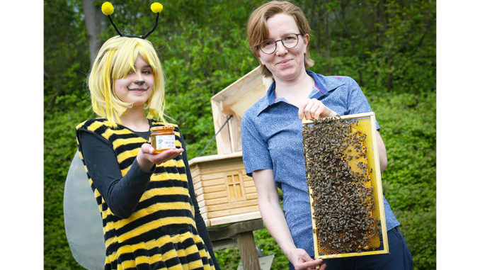 Ida (12; links) mit für die Premiere produzierten Honig und Imkerin Sandra Denker mit einer Bienenwabe aus dem dahinter zu sehenden Schaukasten. // Foto: Anke Hesse